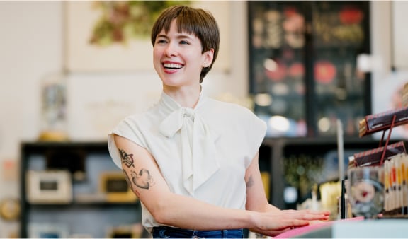 A smiling woman stands next to a counter in a shop.